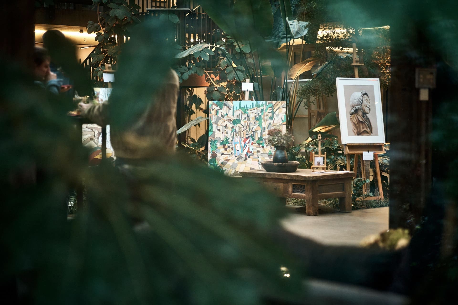 artmosphere Vol 2: Werke auf Staffeleien im Atrium des Innergarden, durch die Pflanzen gesehen