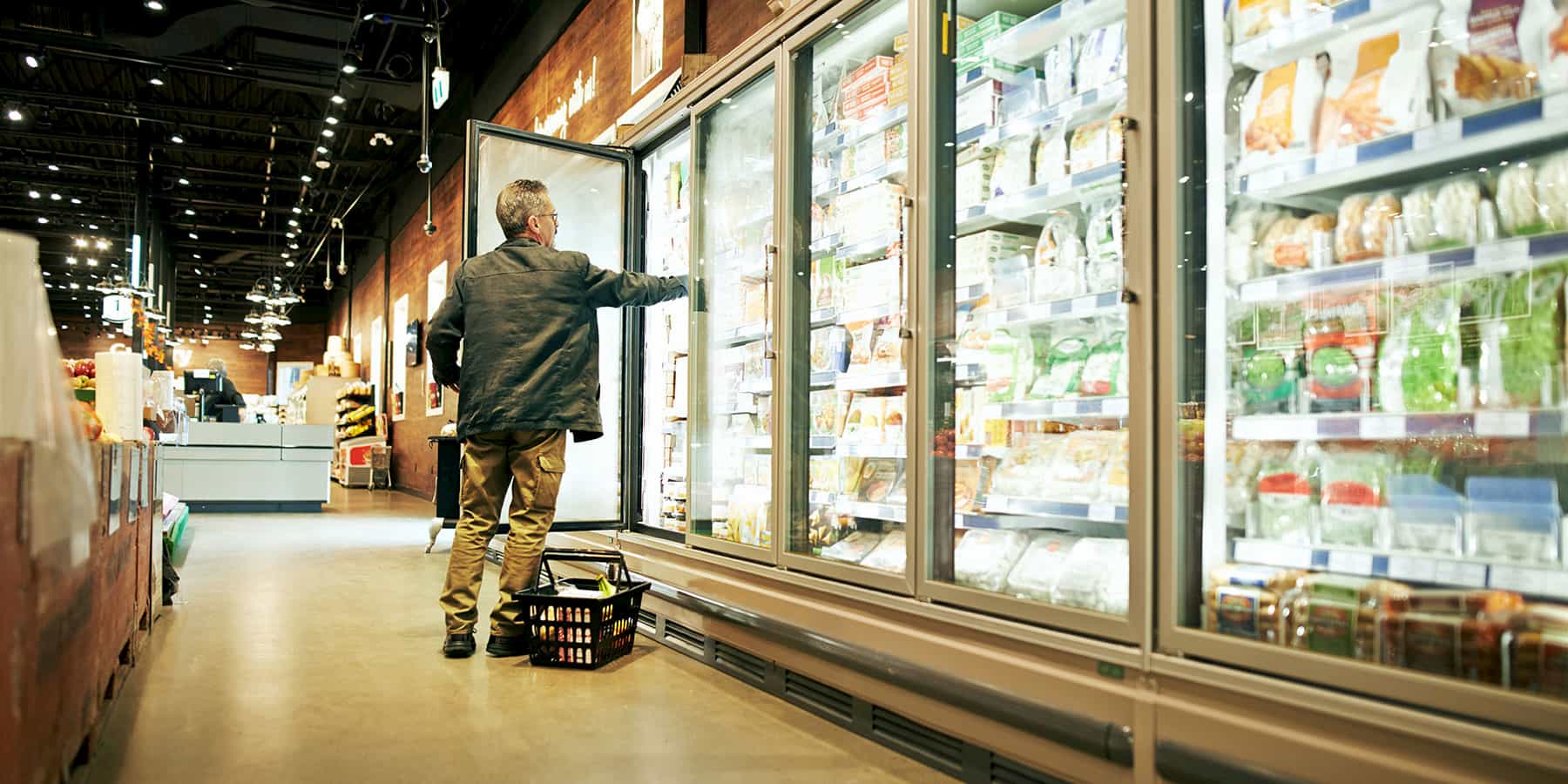 Man shopping in grocery story frozen aisle taking picking something out of the freezer shelf