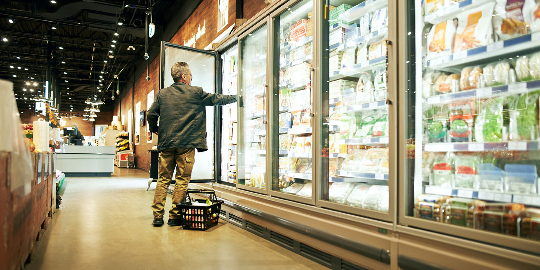 Man in grocery store freezer aisle opening freezer door to take product.