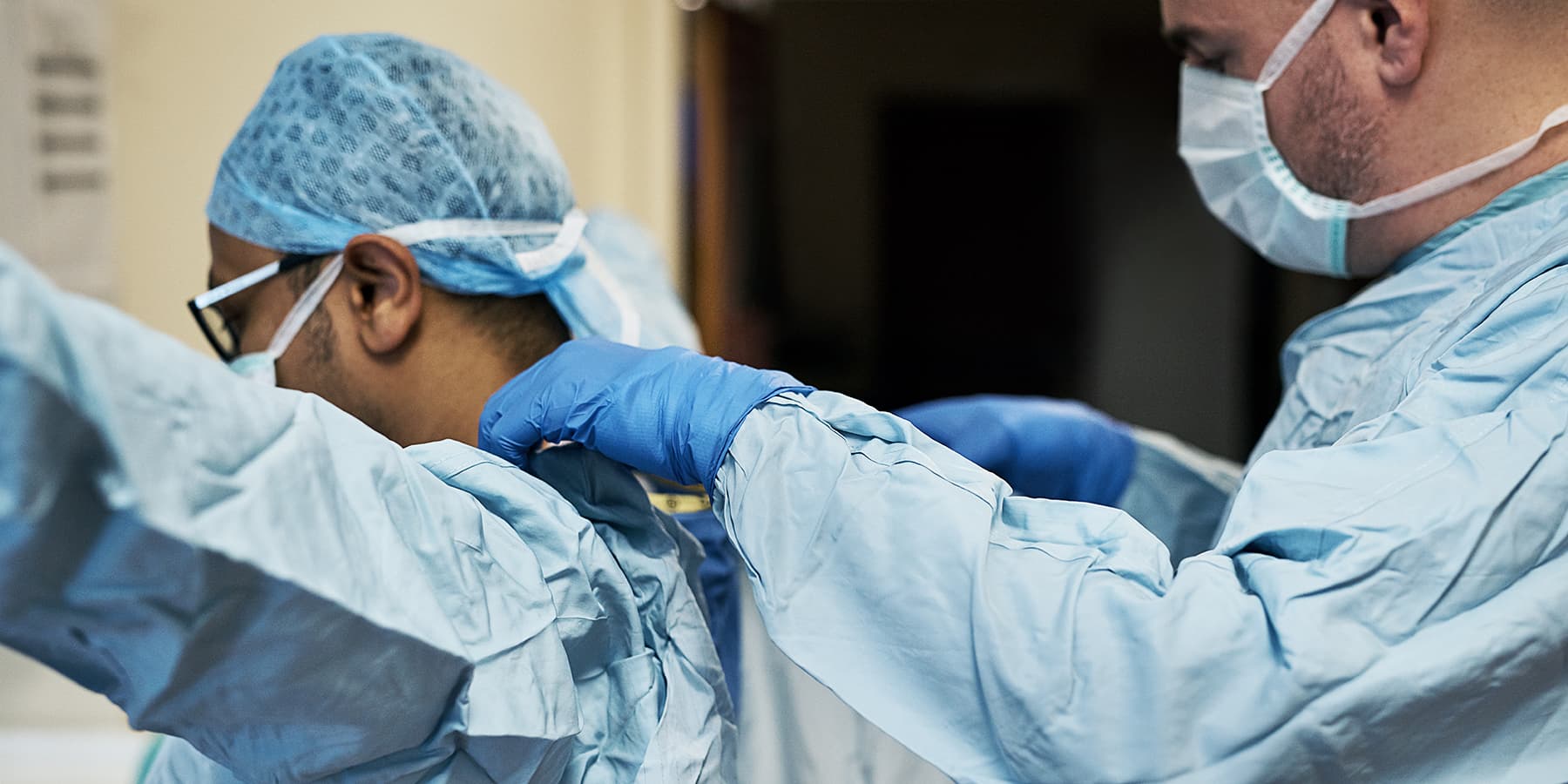 One doctor helping another doctor put on surgical scrubs