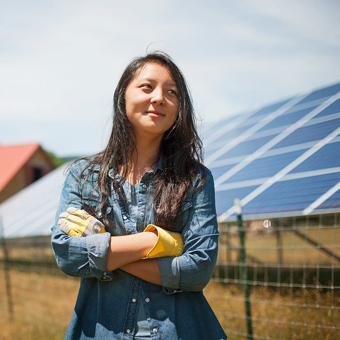 Woman standing proudly in front of solar panels with their work clothes on.