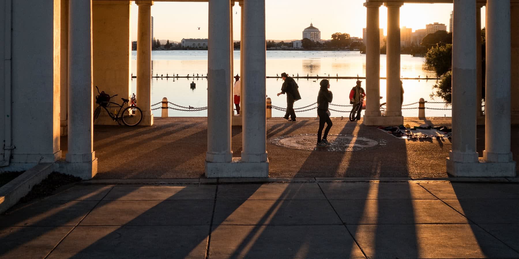 View of people walking under pillars by a lake in the sunset