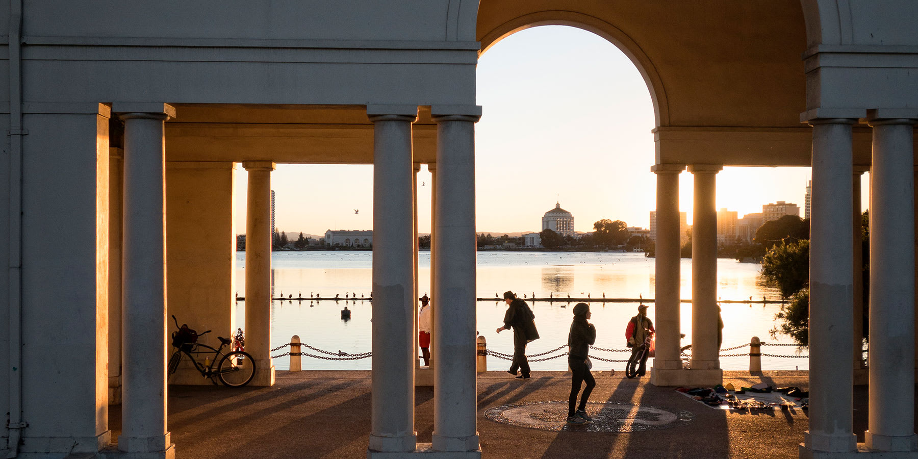 People walking through arch next to Lake Merritt at sunset