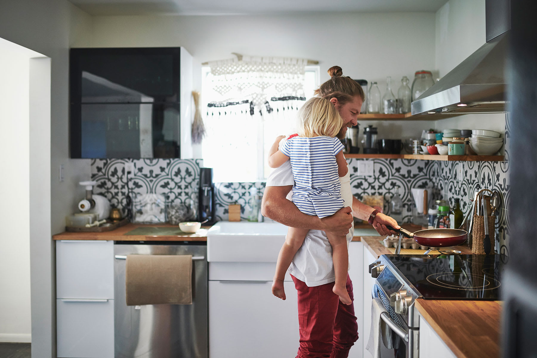 Father holding his daughter in the kitchen while cooking on an induction stovetop.