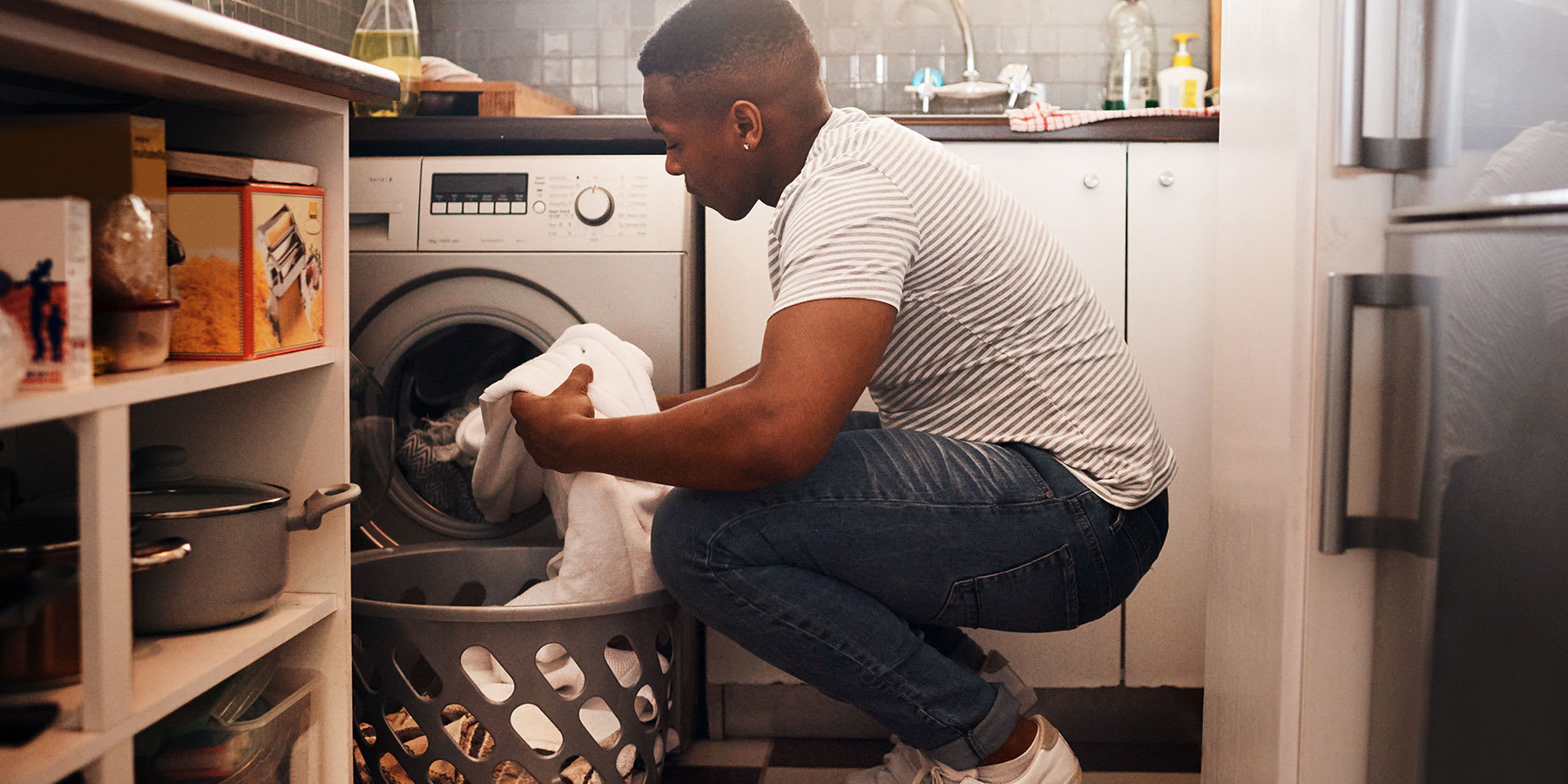 Man in his mid-20s loading the washing machine in his apartment