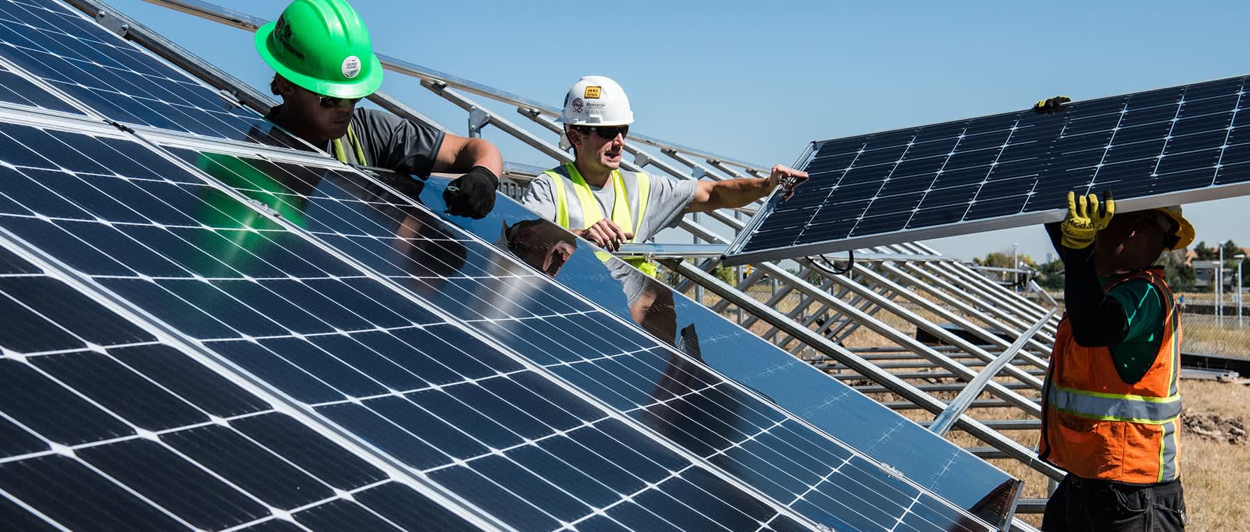 Three workings putting up solar panels in a field.