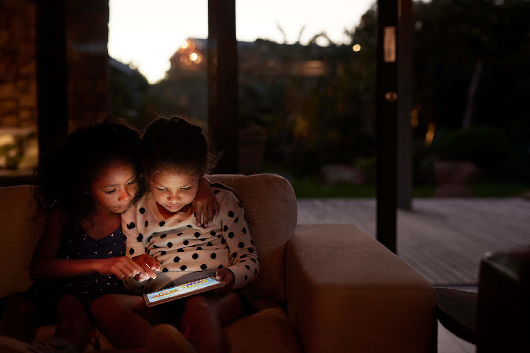 Two young girls looking at their tablet in a dark house