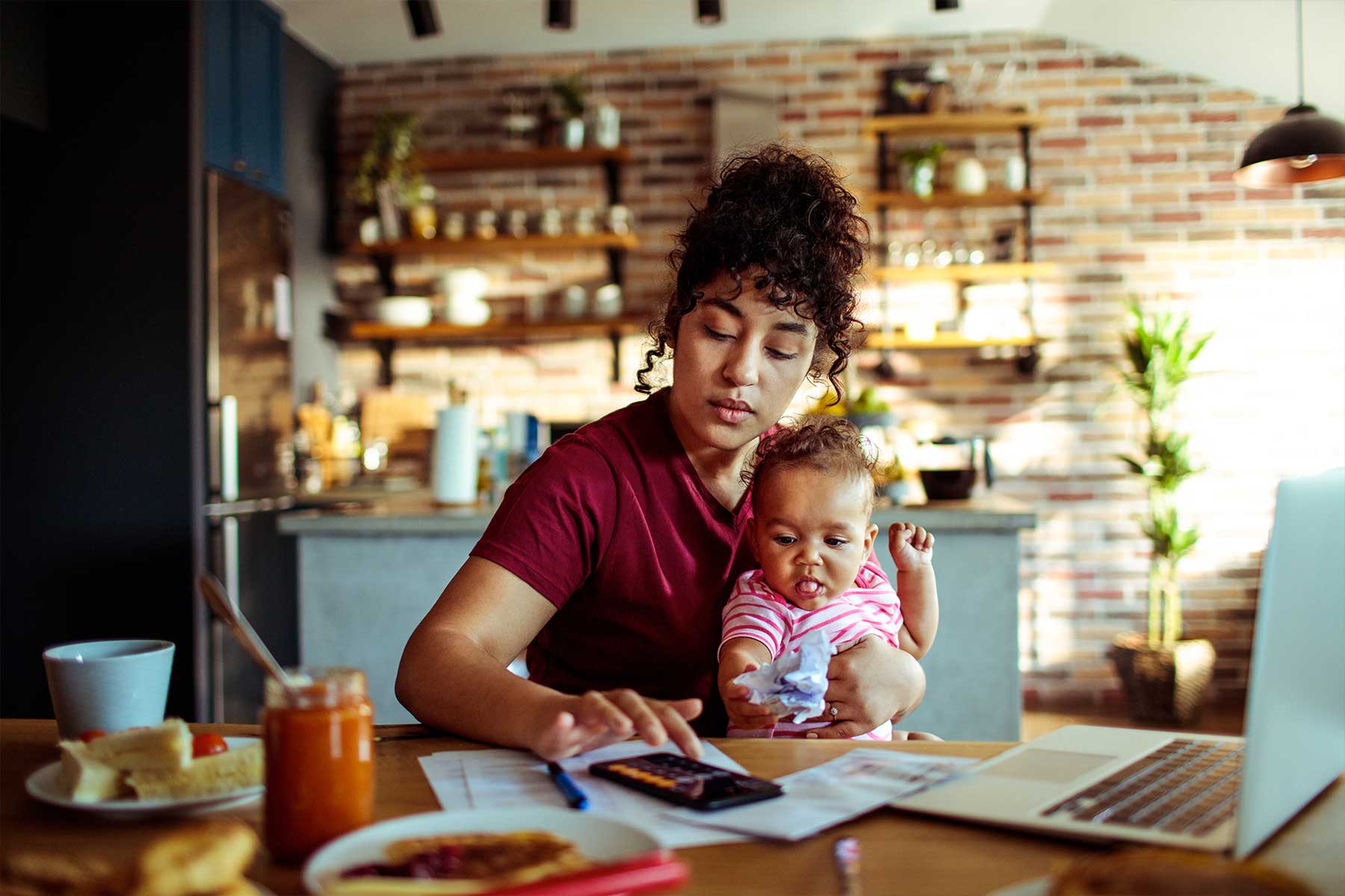 Woman holding a baby while paying bills on her computer at a table