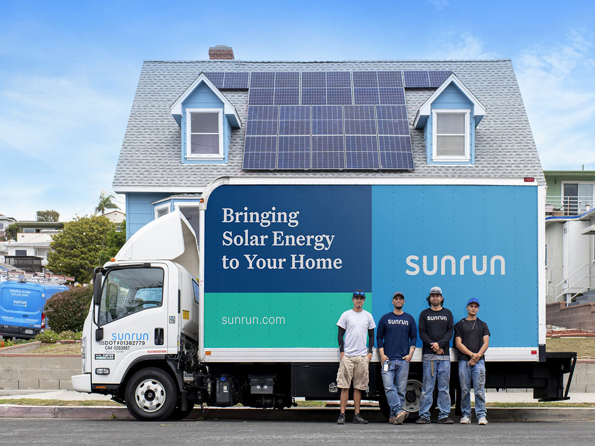 Sunrun employees in front of a Sunrun truck parked in front of a home with solar panels installed