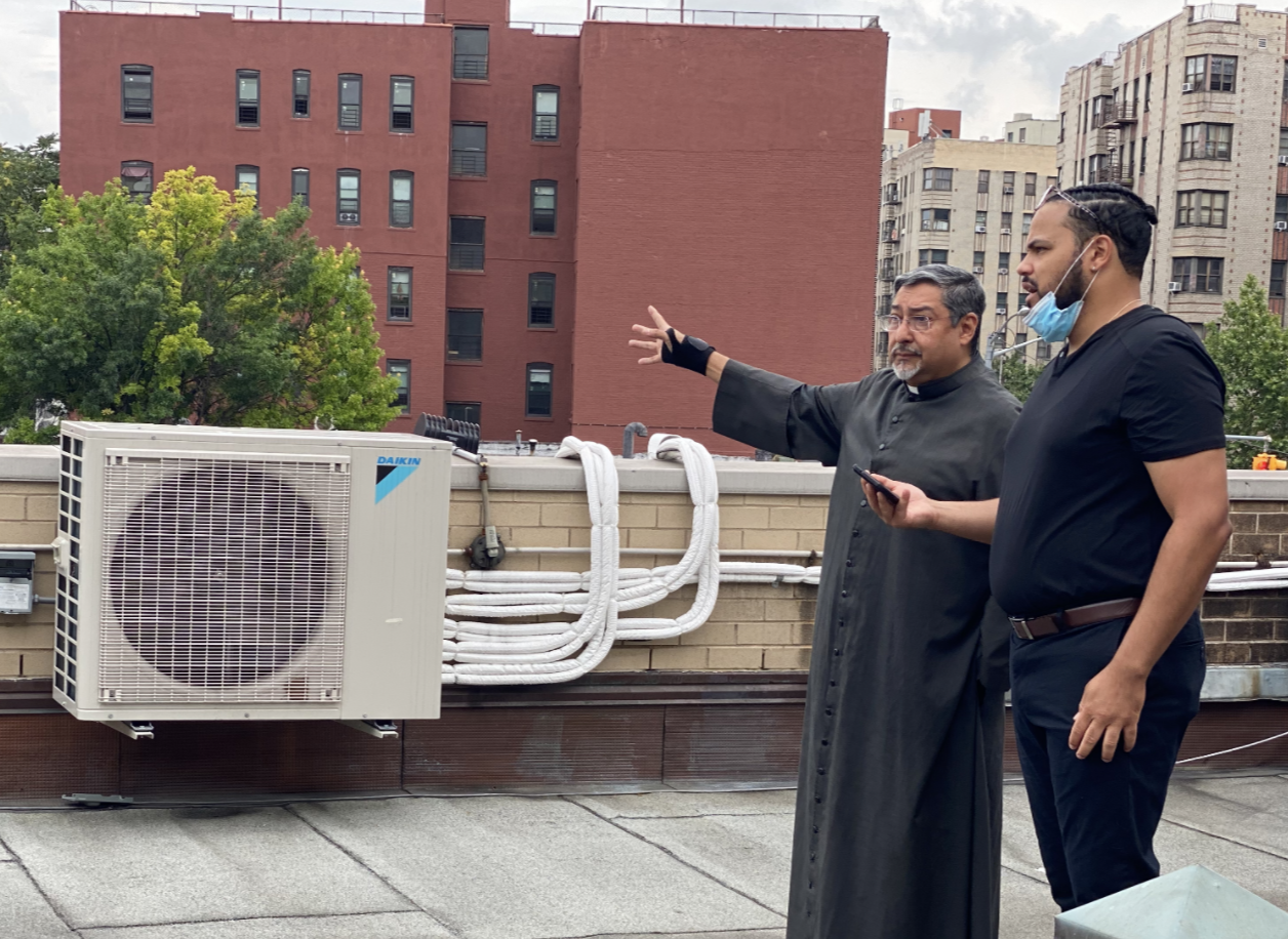 Two men on a roof looking at a heat pump