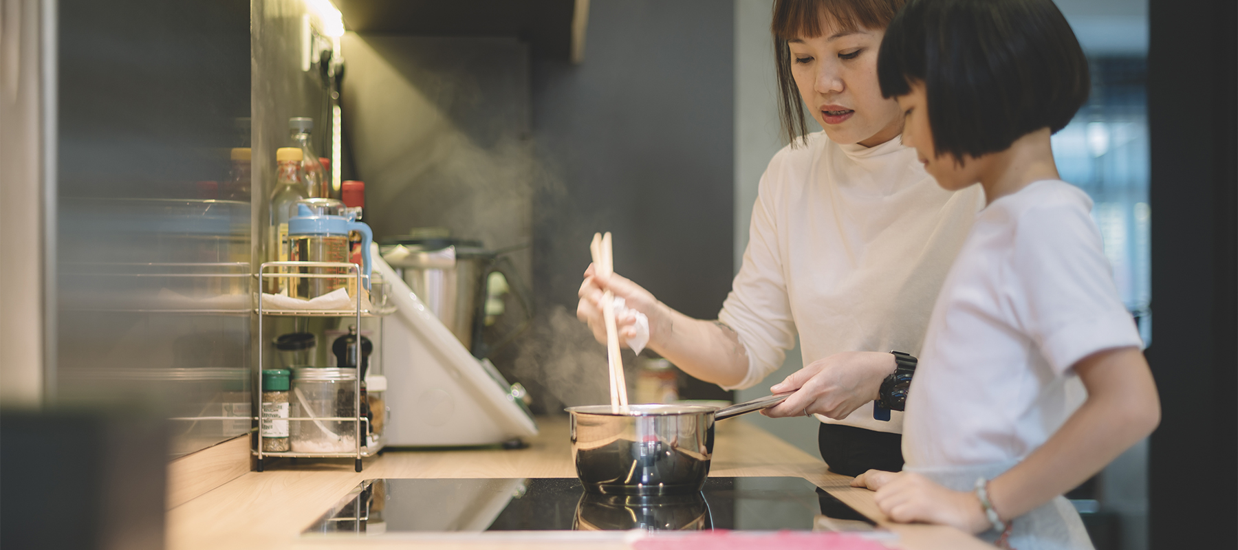 Mother teaching young daughter how to cook on an induction stove.