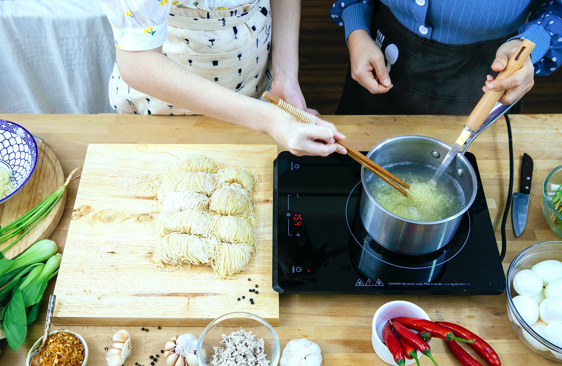 Hands cooking a noodle soup on an induction burner
