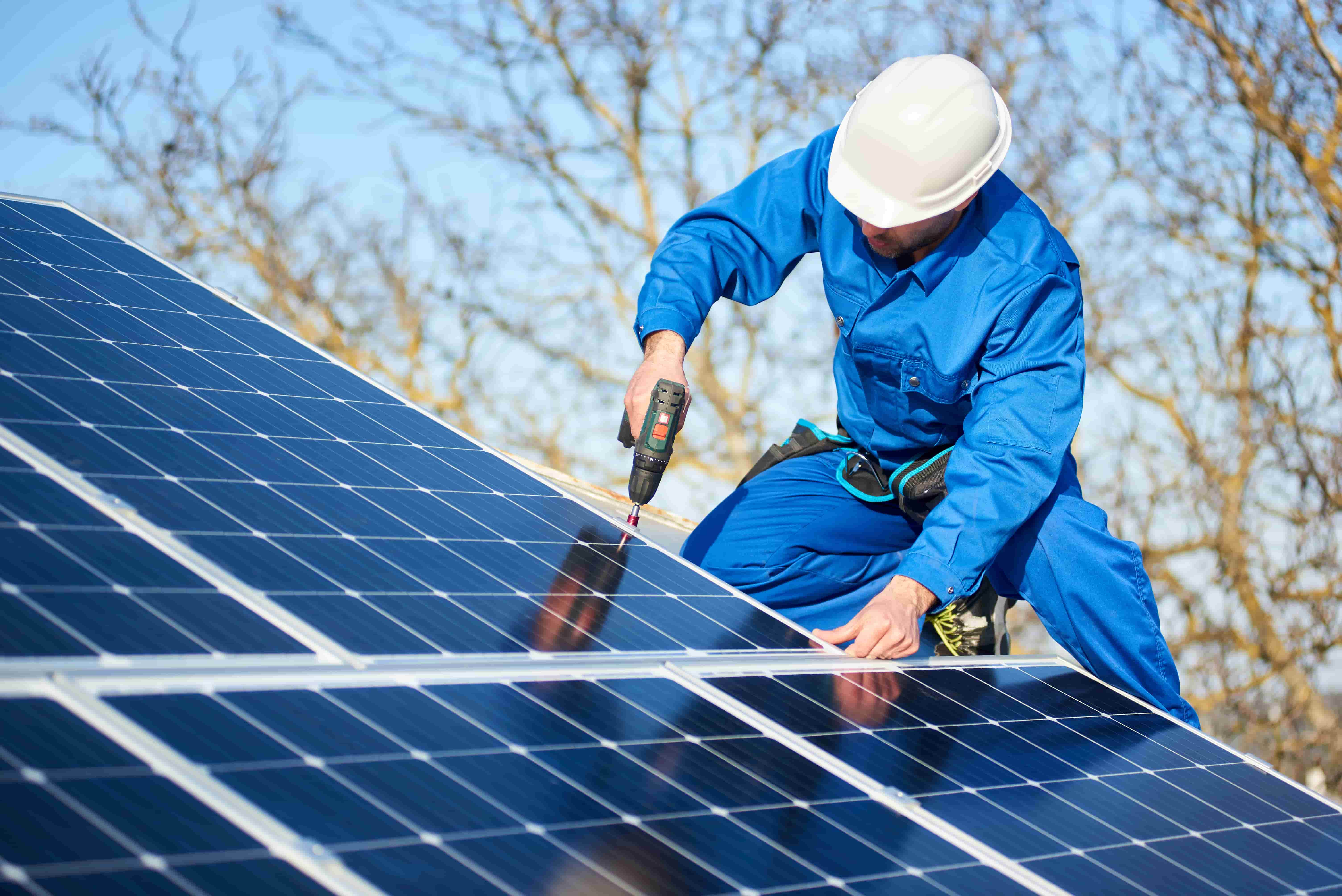 Man in blue uniform using a drill to install solar panels