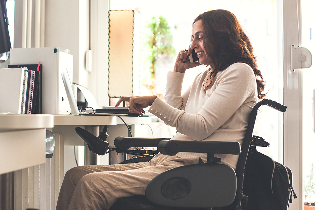 Woman in a wheelchair talking on a cell phone while using her computer
