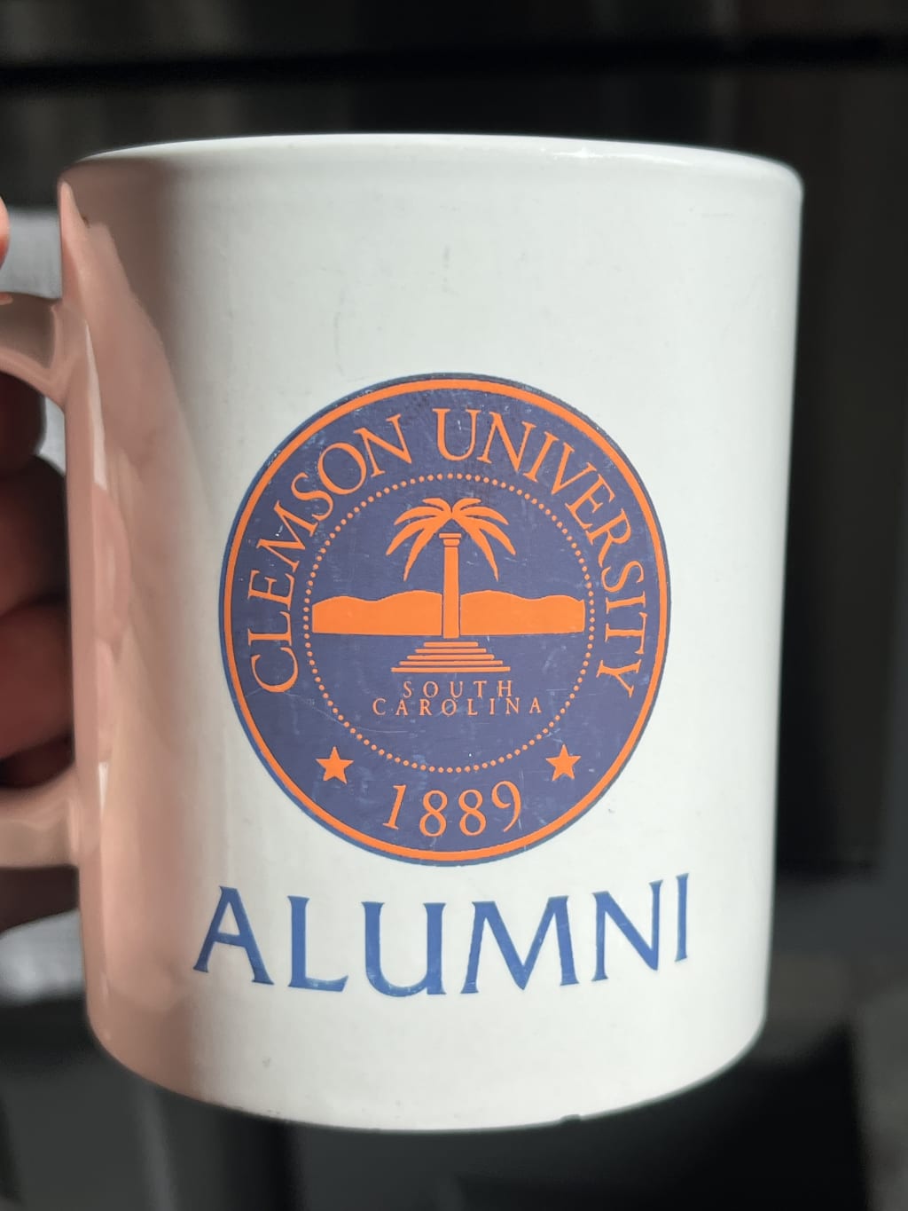 White ceramic Clemson University alumni mug with orange and blue logo and text.