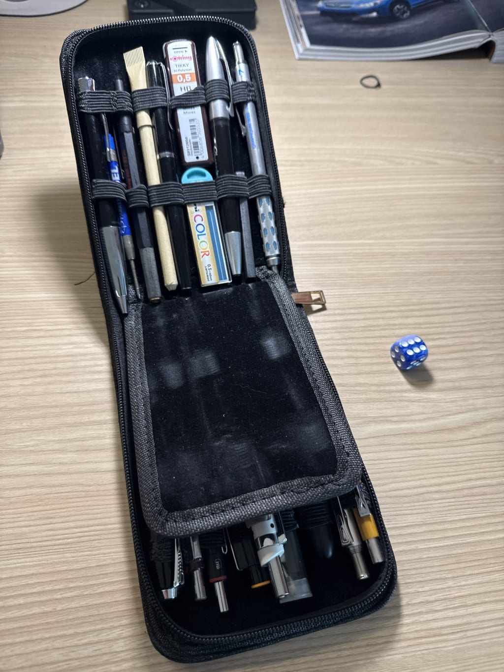 A black pencil case containing various writing tools and two packs of 0.5mm leads.