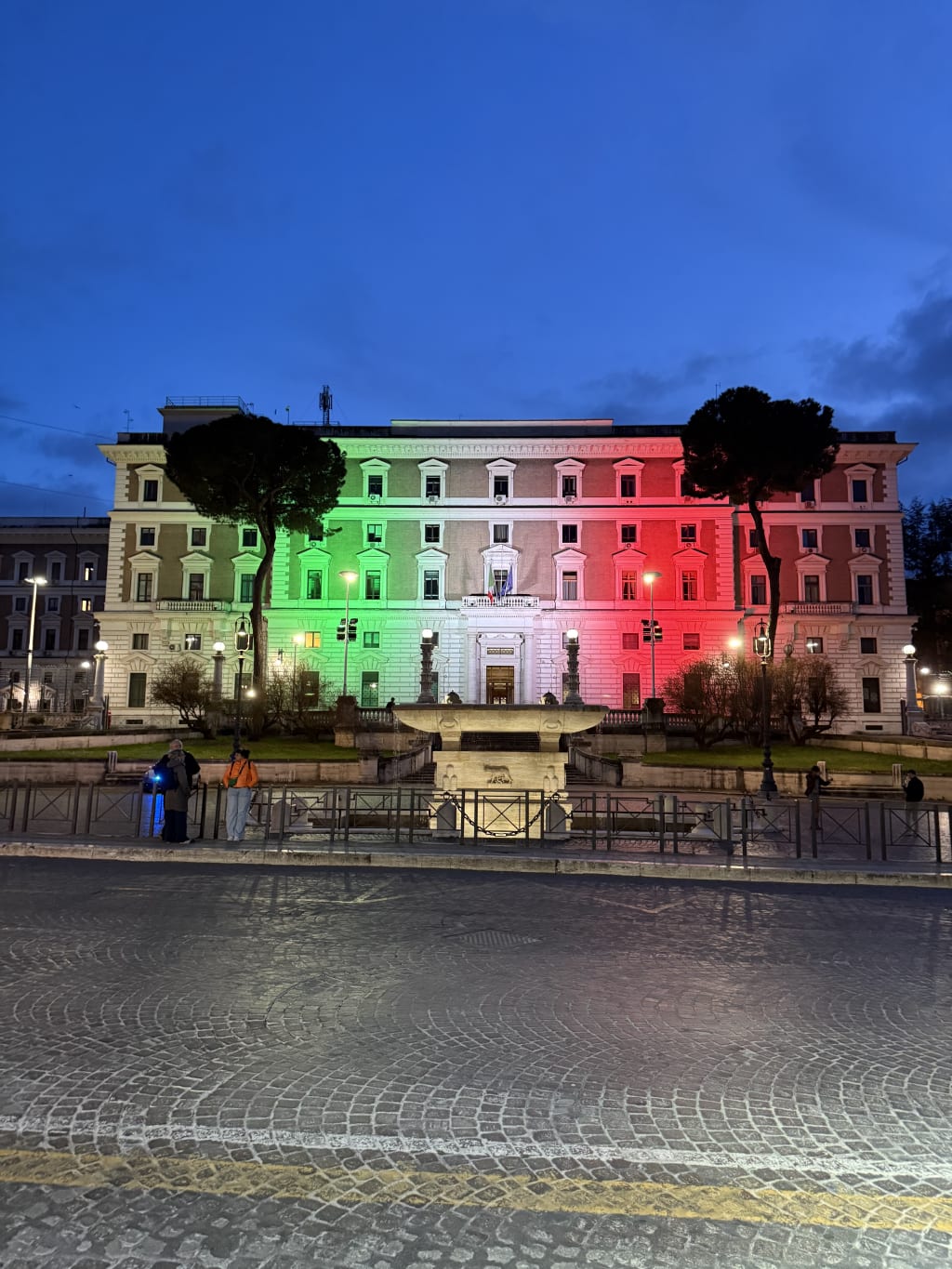The Viminali historic building illuminated with green, white, and red lights resembling the Italian flag at dusk.