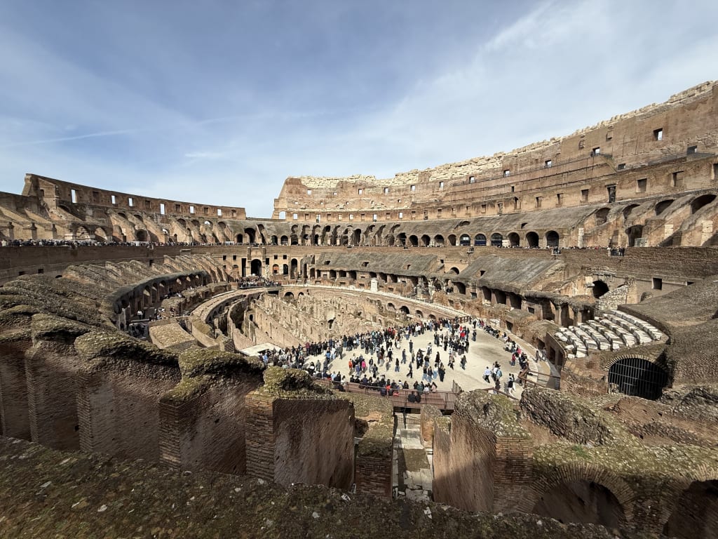 A wide view of the Roman Colosseum's interior with tourists exploring the ancient amphitheater.