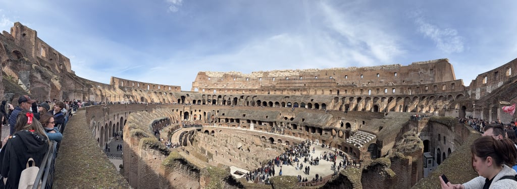 Panoramic view of the interior of the ancient Roman Colosseum with tourists inside.