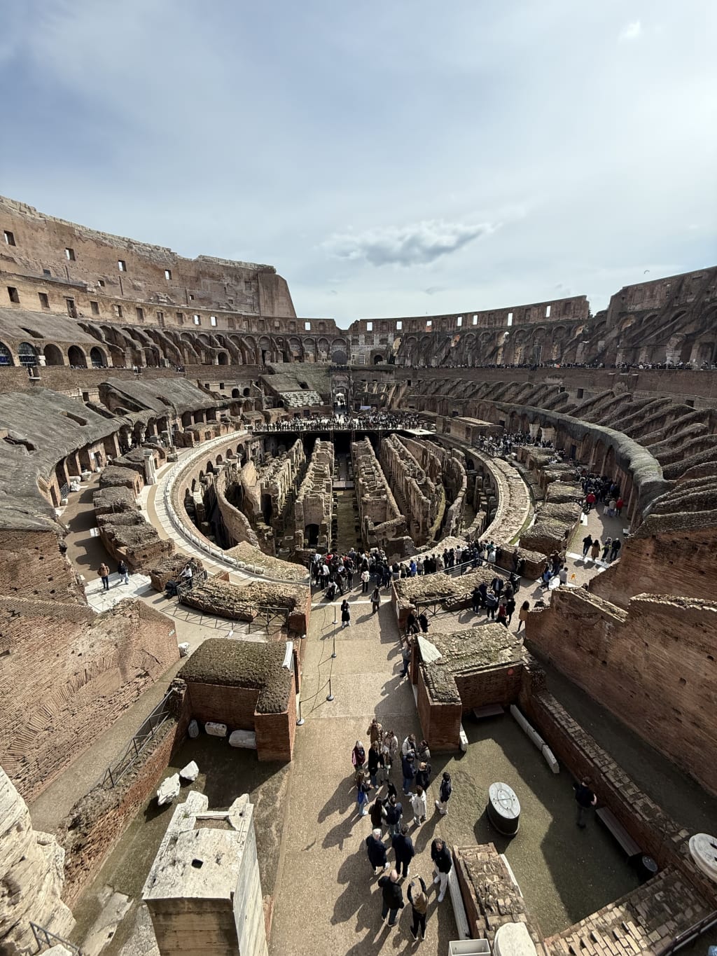 Interior view of the Colosseum in Rome, showing ancient stone architecture and tourists inside.
