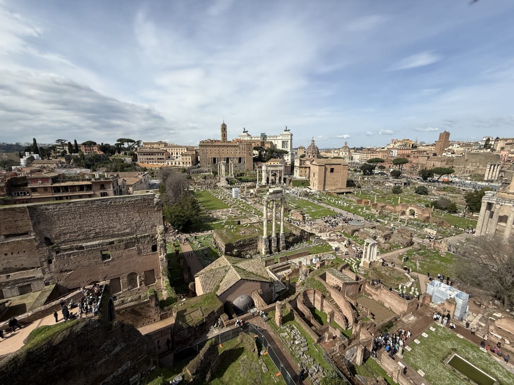 Aerial view of ancient Roman Forum ruins with visitors exploring the historical site in Rome.