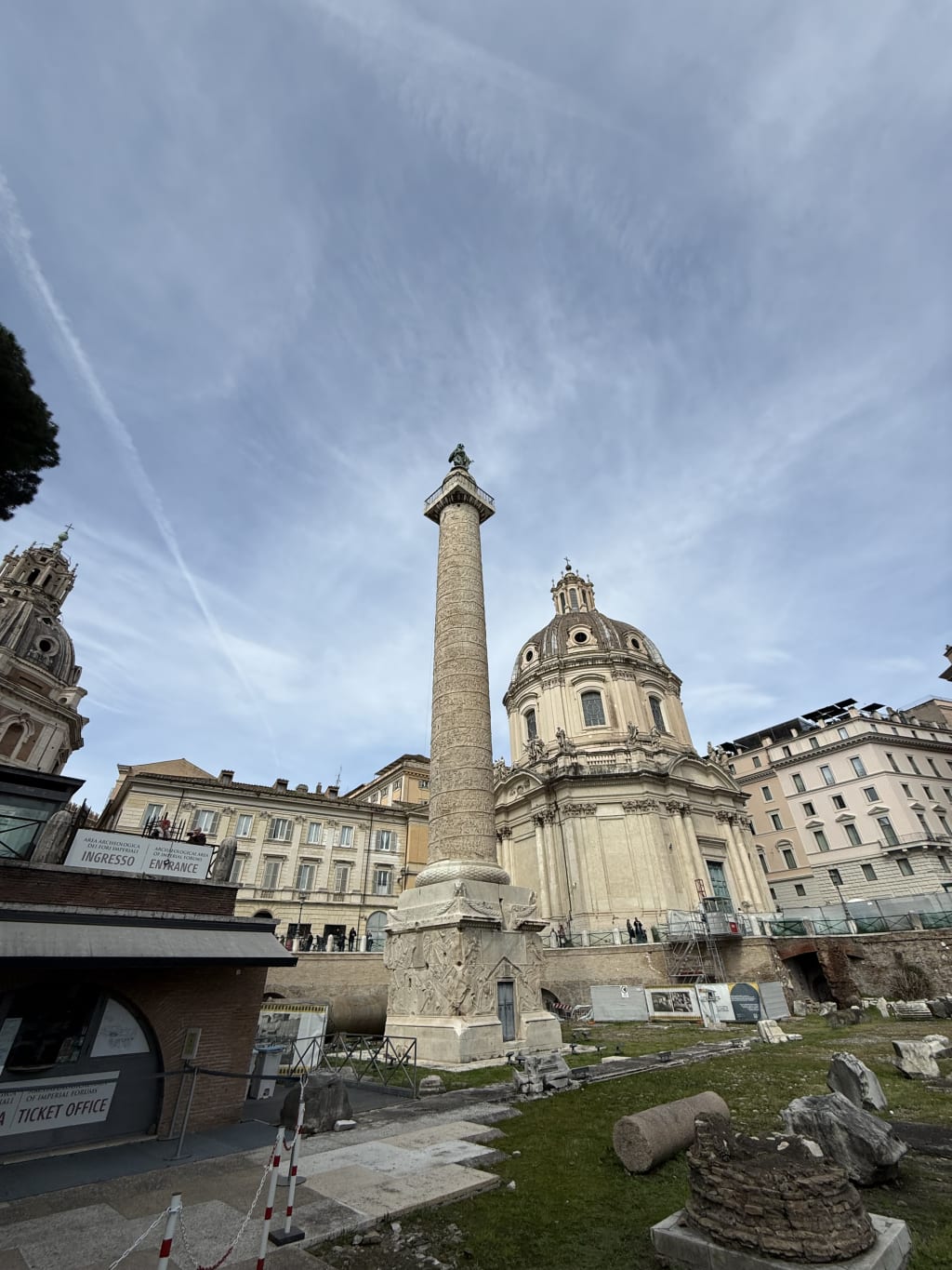 The Column of Trajan in Rome stands tall with intricate carvings and nearby historic buildings.