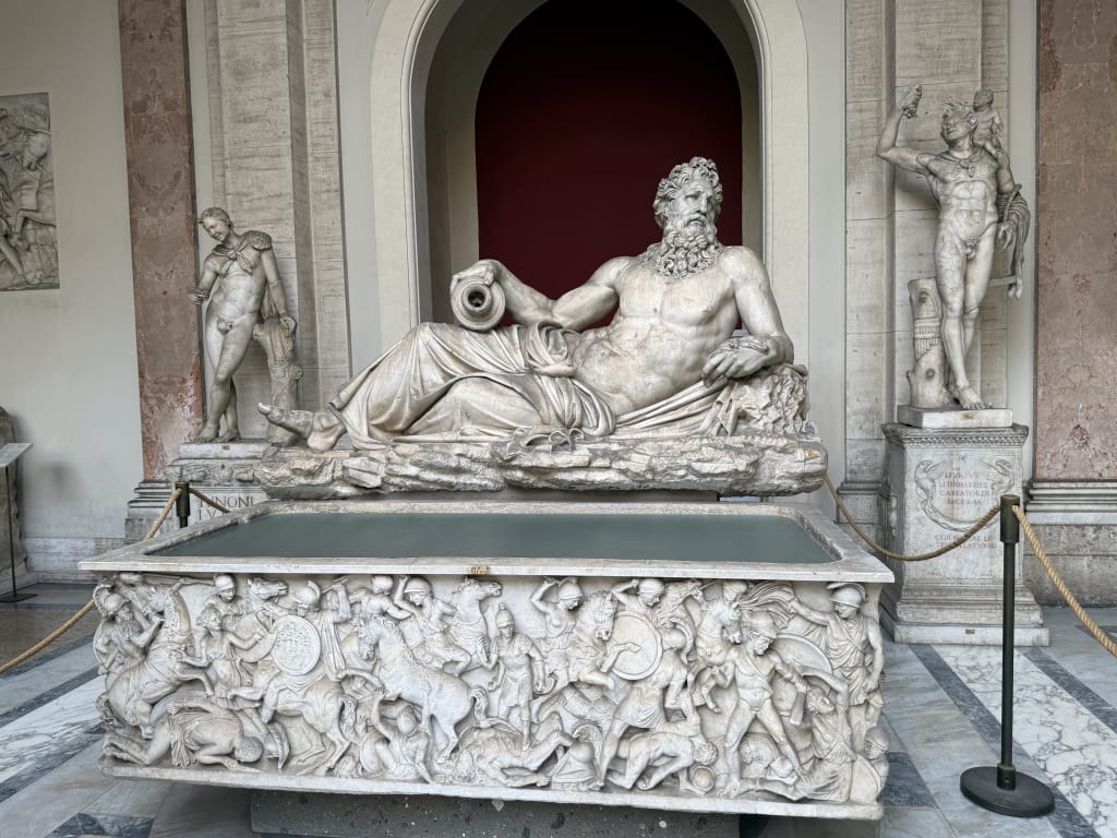 This image shows an intricately carved marble sarcophagus with a reclining bearded male statue on top.