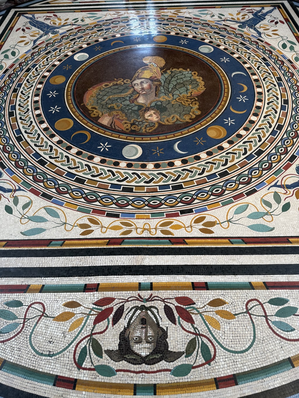 Intricate mosaic floor featuring a central figure with cosmic symbols and decorative foliage designs.