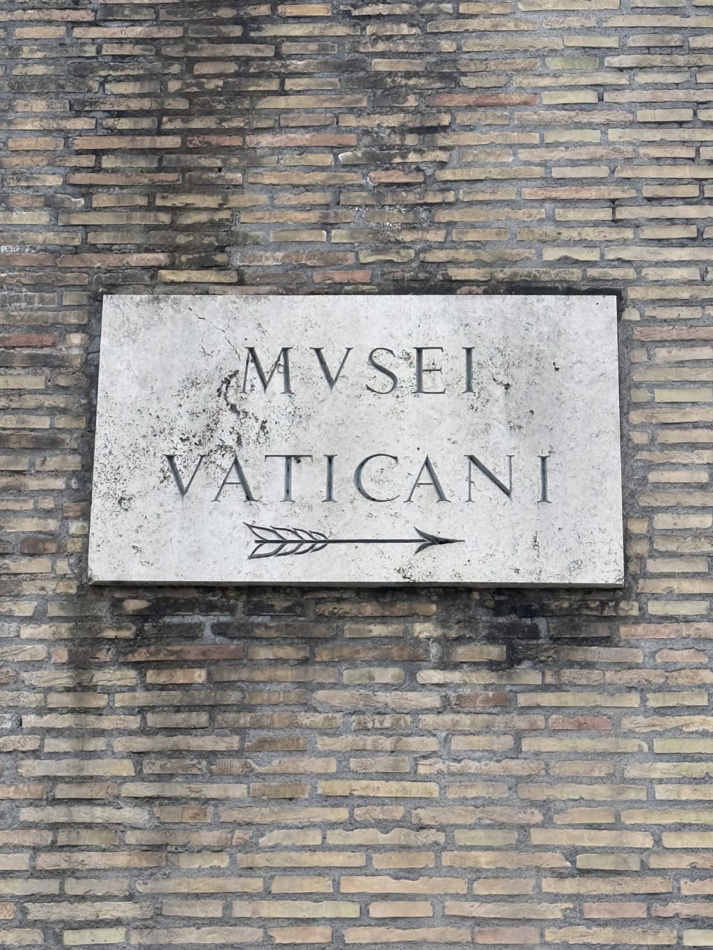 A stone plaque on a brick wall with the inscription "MUSEI VATICANI" and an arrow.