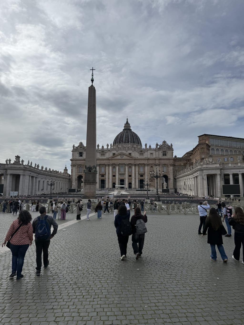 Tourists walk towards St. Peter's Basilica and the Vatican Obelisk in St. Peter's Square, Vatican City.