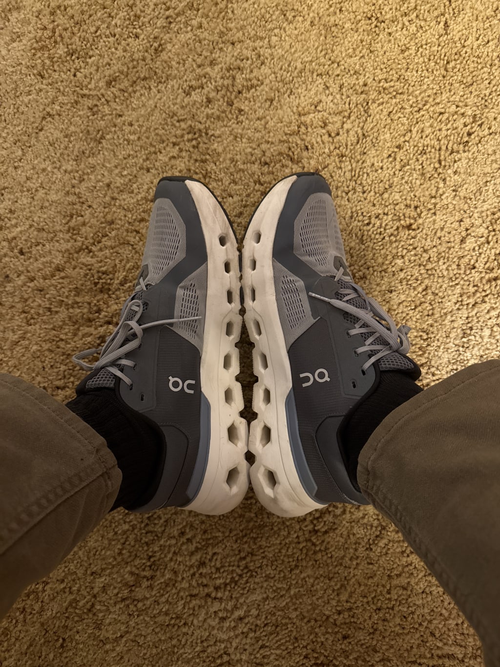 Person wearing gray On running shoes with white soles on a textured carpet.