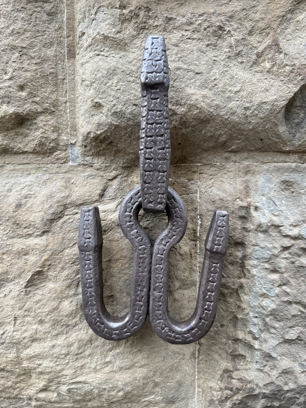 A close-up of a decorative iron hook mounted on a textured stone wall.