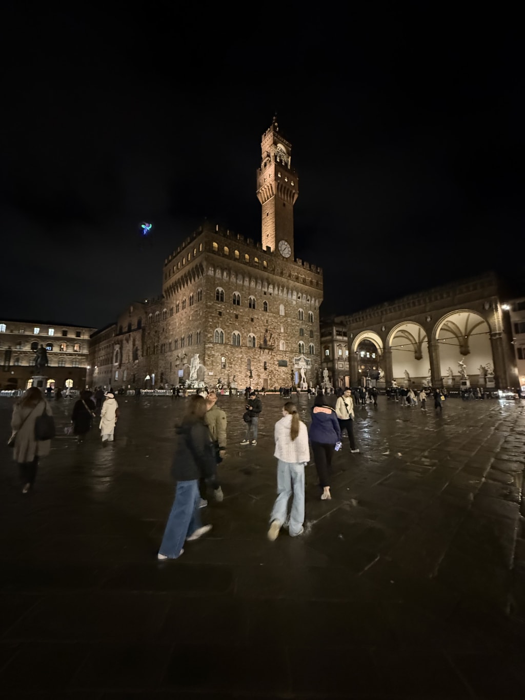 Maia, Sofia and Anca walking in Piazza della Signoria at night with Palazzo Vecchio illuminated.