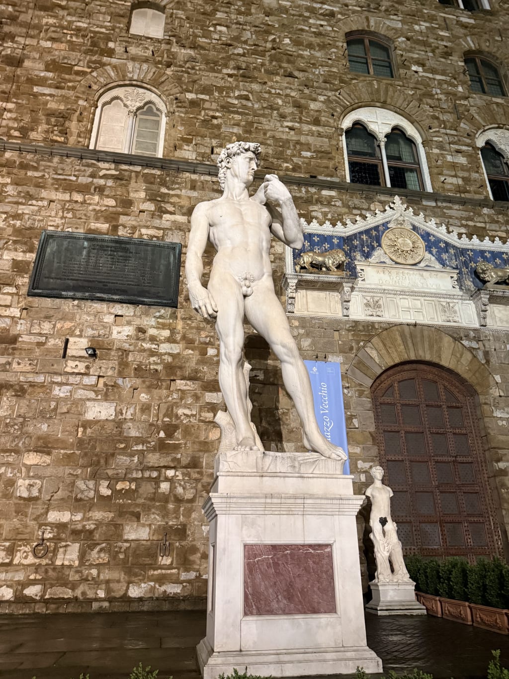 The statue of David stands illuminated at night outside the Palazzo Vecchio in Florence.