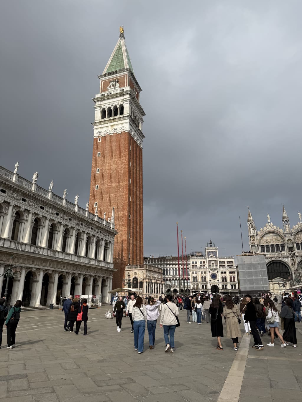 Crowd walking near the Campanile di San Marco under a cloudy sky in Venice.