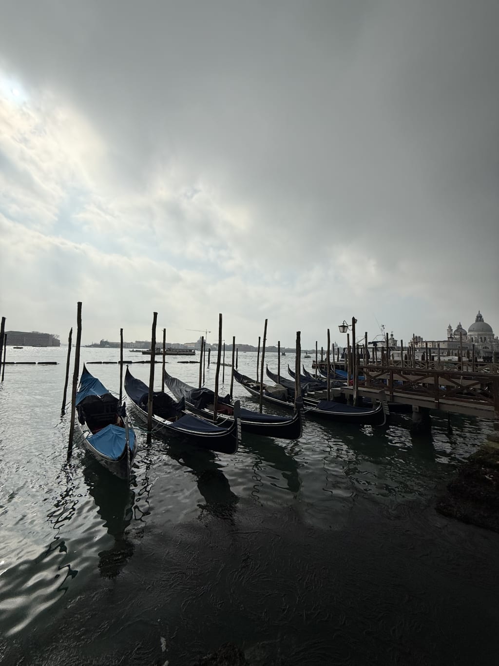Gondolas moored along wooden posts on a cloudy day in Venice, Italy.