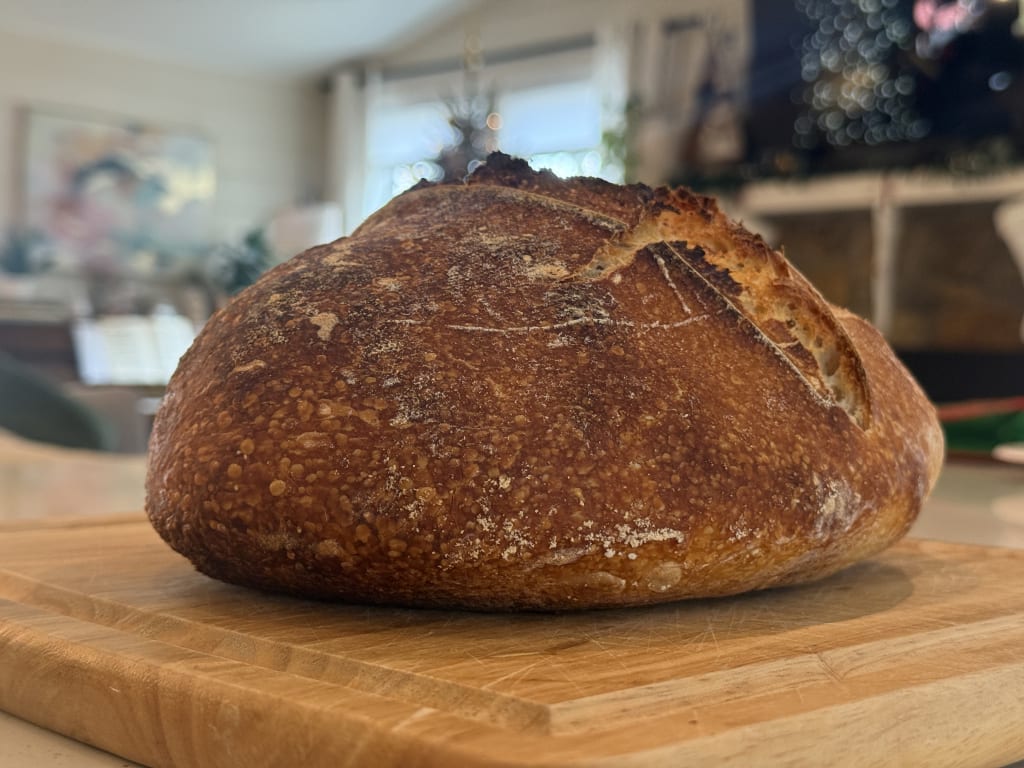 A freshly baked round loaf of sourdough bread resting on a wooden cutting board.
