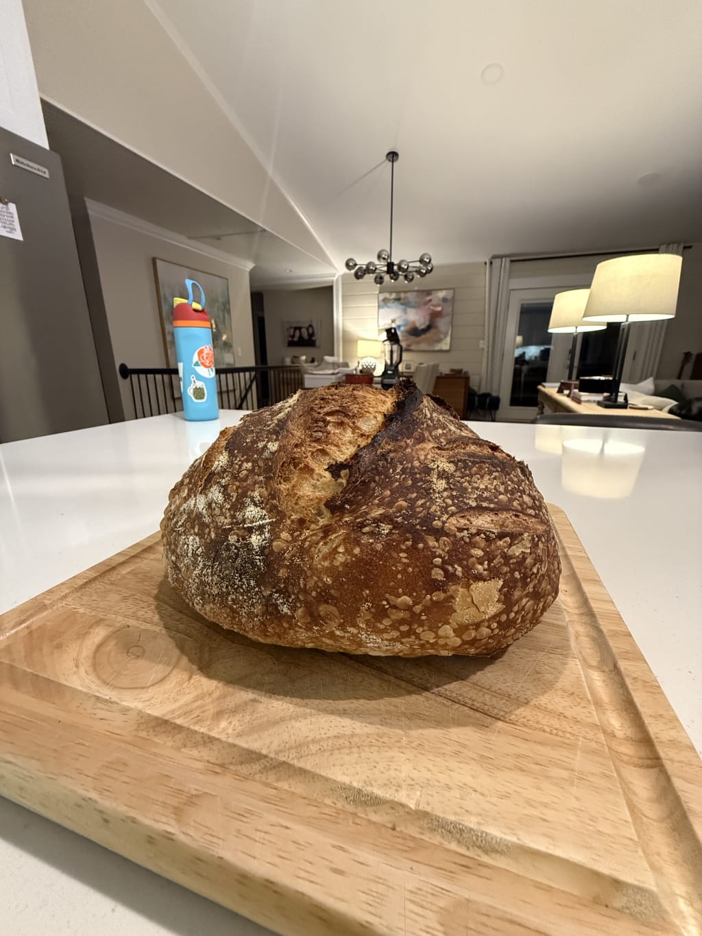 A freshly baked loaf of crusty sourdough bread rests on a wooden cutting board.