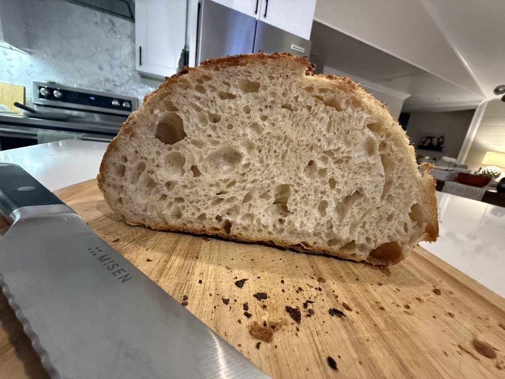 Freshly sliced artisanal bread on wooden cutting board with serrated Misen knife.