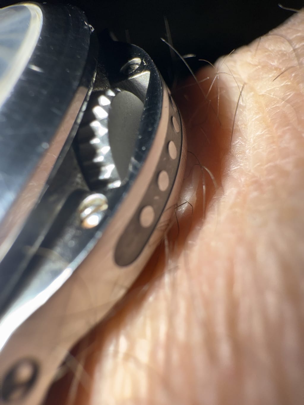 Close-up of a metallic watch bezel on a wrist, highlighting detailed grooves and texture.