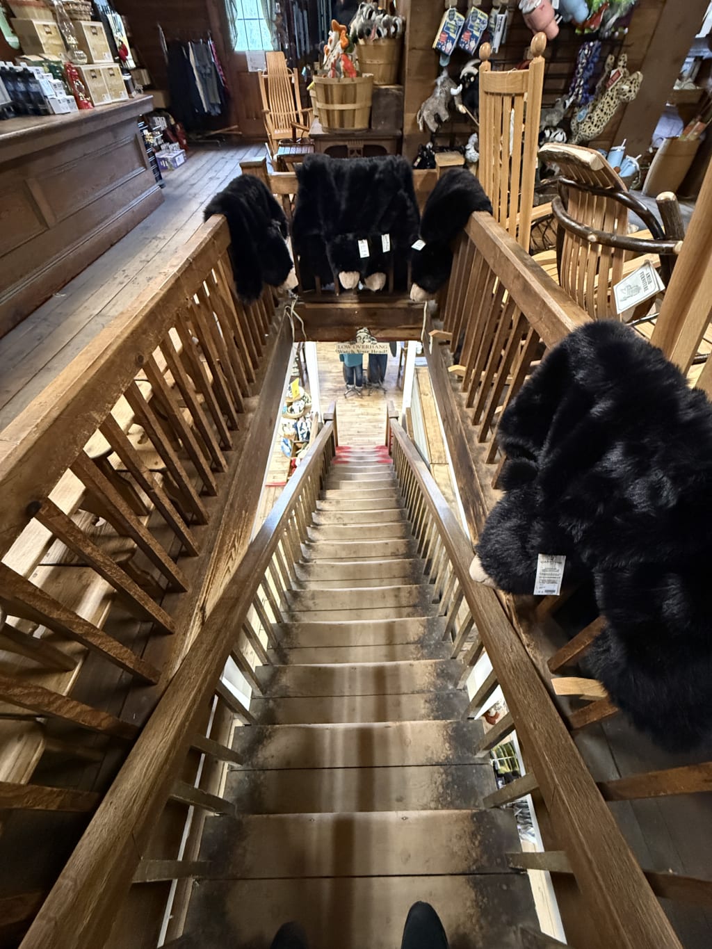 A narrow wooden staircase with black fur throws draped over the banisters inside a rustic shop.