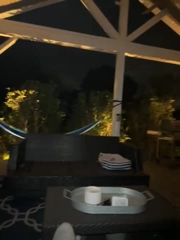 A nighttime outdoor seating area with a cushioned chair, table, and folded blankets.