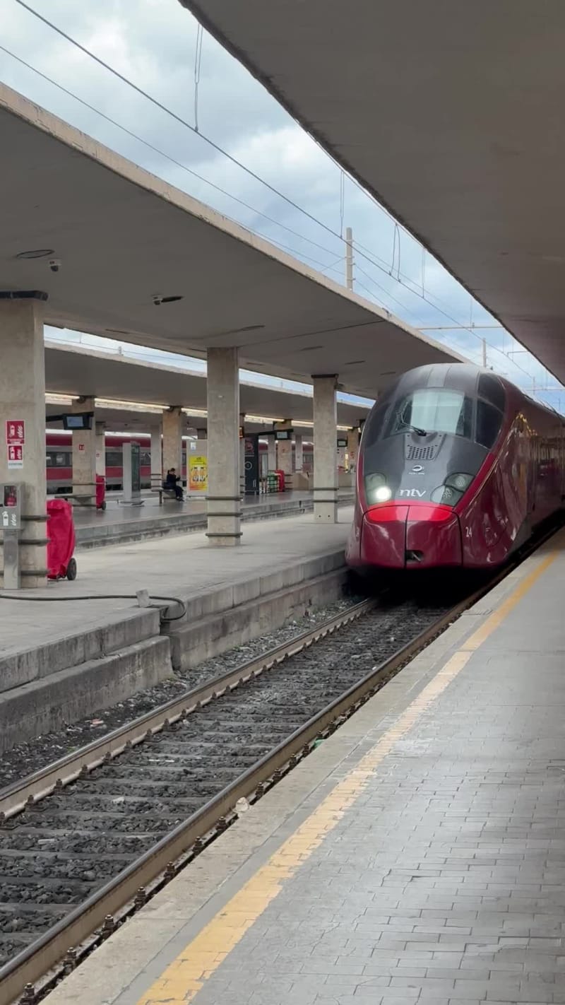 A sleek red and black train is arriving at a platform in the Florence train station.