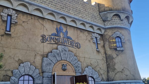 Fantasy castle-style exterior with arched stonework, small blue-framed windows, and a carved bear head above an arched doorway; weathered, beige wall.