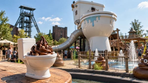 Chocoladesoftijs in een klein wc-potje, met een reusachtige toiletpot, glijbaan en waterspeelplaats op de achtergrond.
