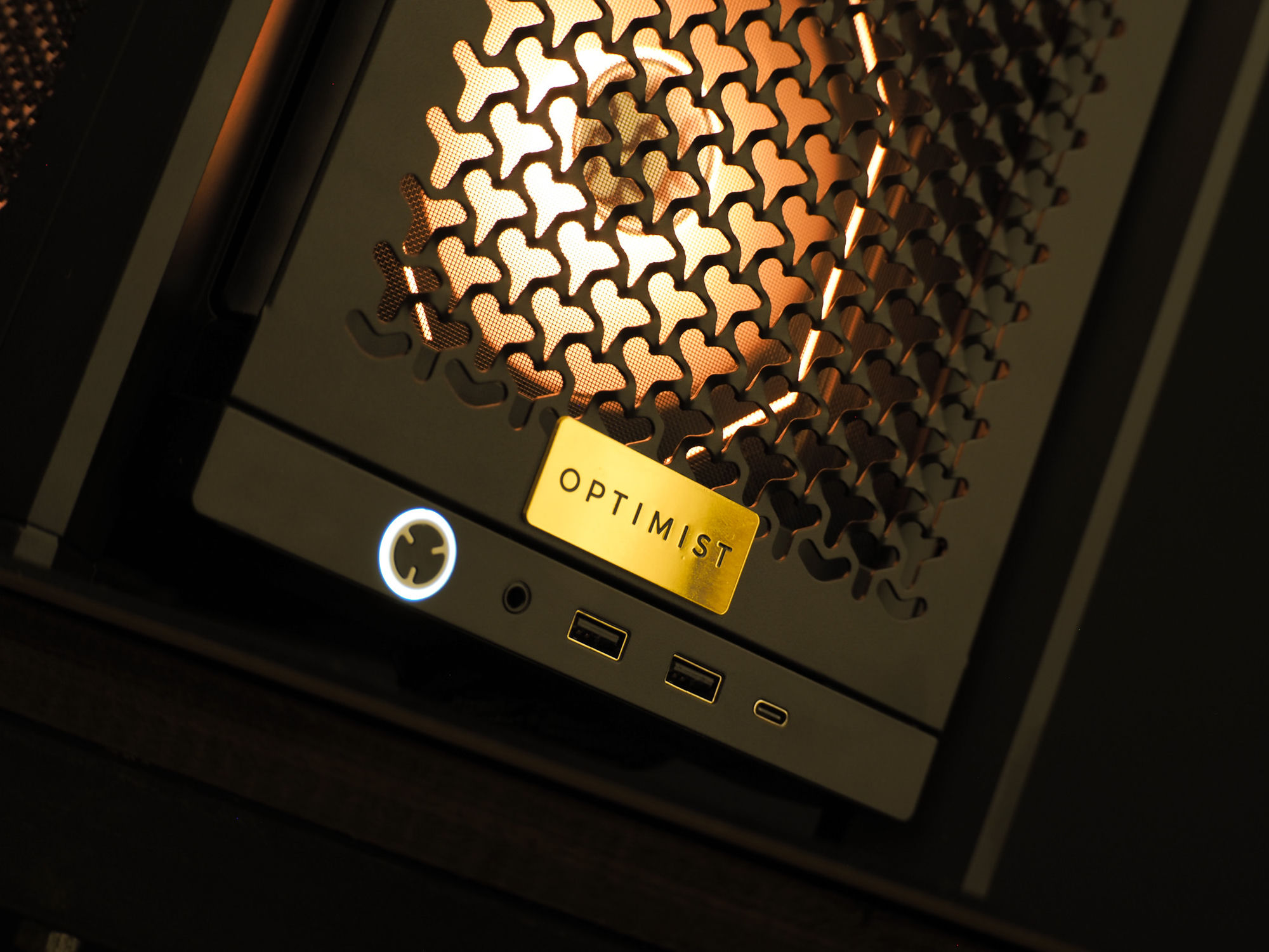 Perforated front panel with a brushed-gold Optimist badge, backlit warm amber