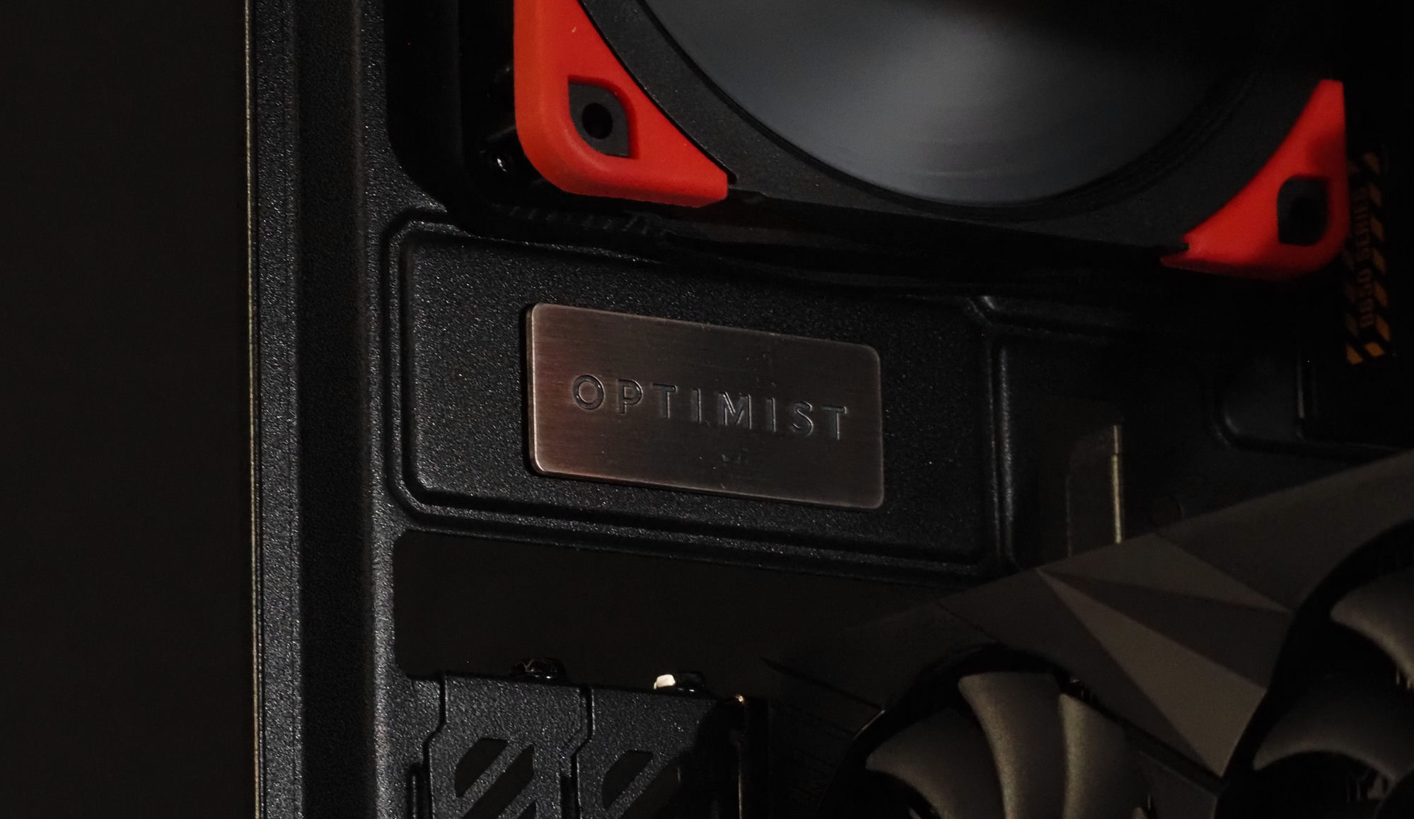 The brushed-metal Optimist badge on the blacked-out chassis, a red fan bumper above it