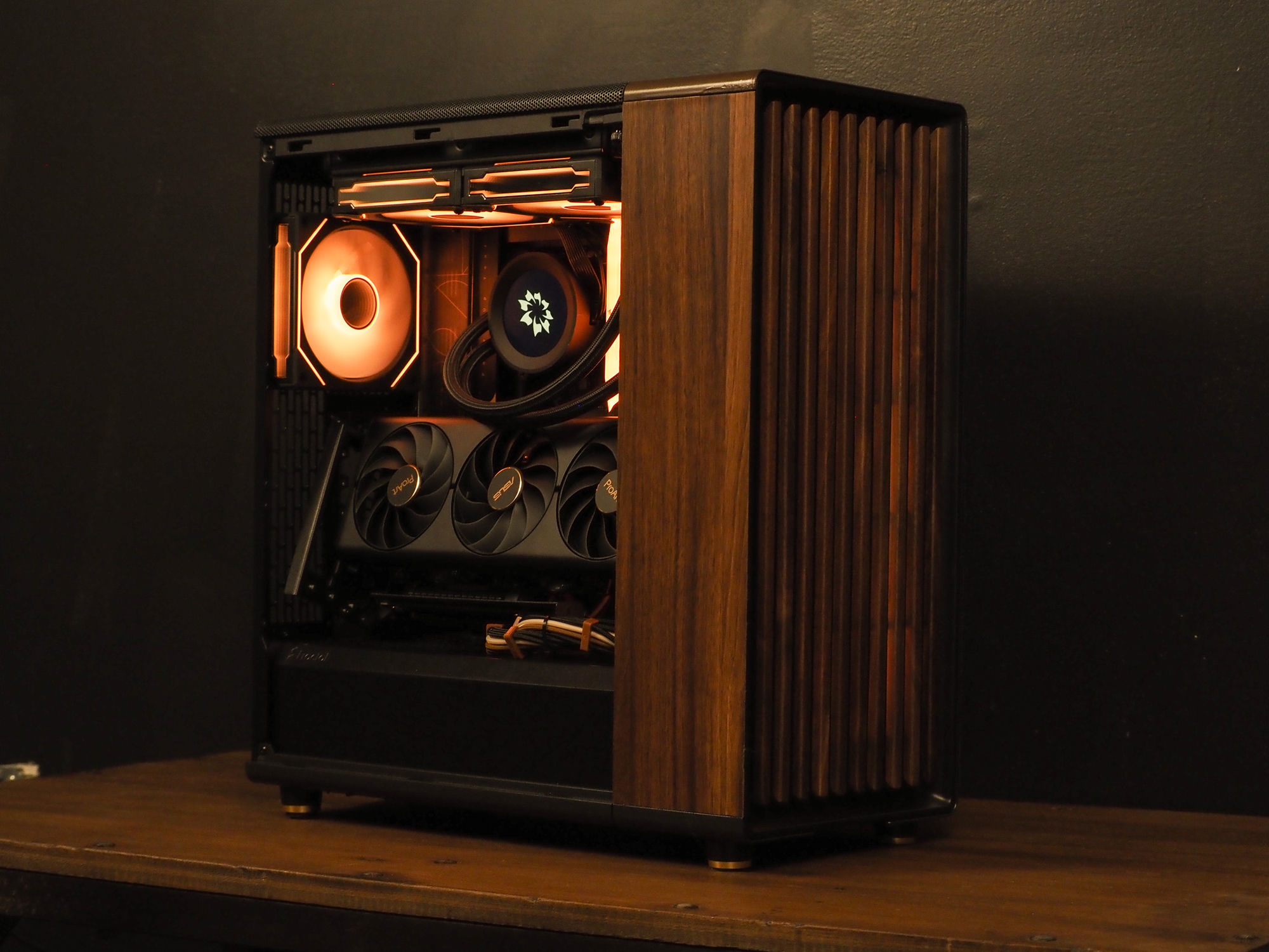 Nocturne — a warm-lit Asus ProArt build with a walnut side panel, calm and furniture-like on a wooden desk