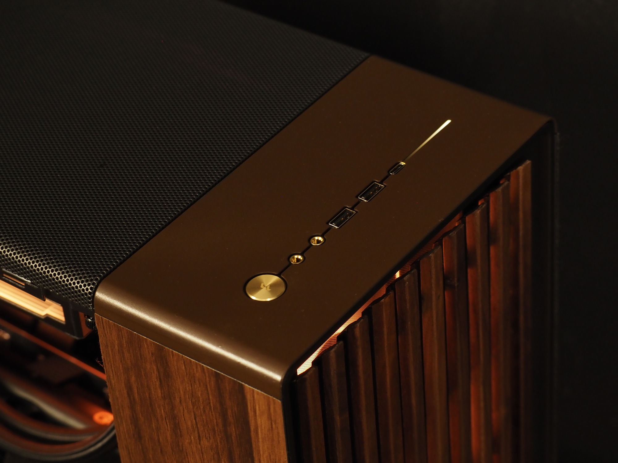 The gold-anodized power button and gold-ringed front I/O ports on the top deck, beside the wood side panel
