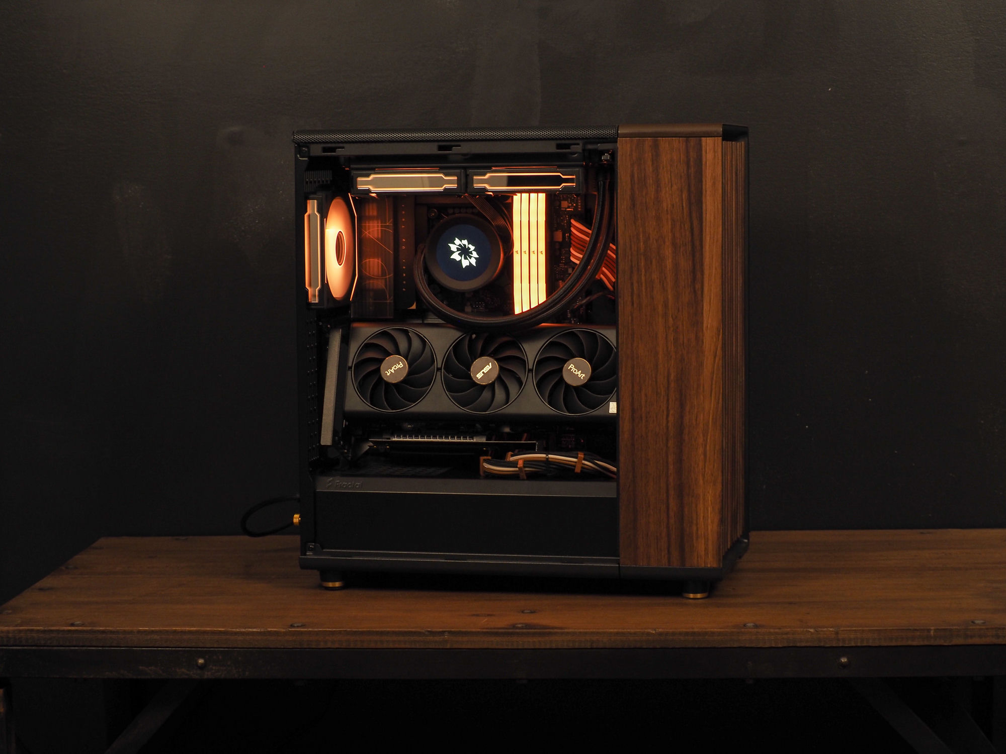 Nocturne — a warm-lit ProArt build with a wood side panel, on a wooden desk against a dark wall